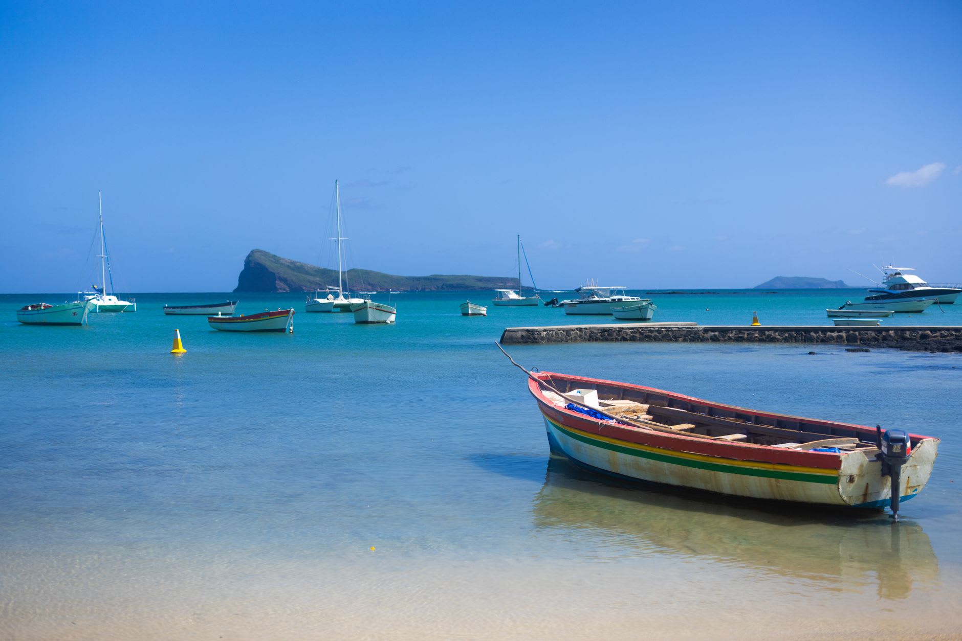 Un catamarán de vela en las aguas turquesas del norte de Grand Baie, la costa de Mauricio visible al fondo bajo el cielo azul