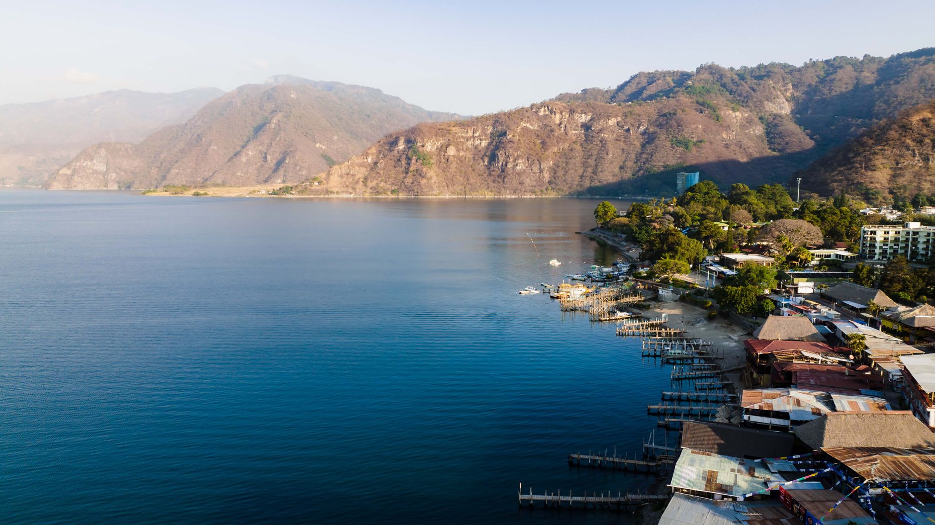 The still surface of Lago Atitlán at dawn from San Marcos La Laguna, a fishing boat silhouetted against the rising light behind the volcanoes