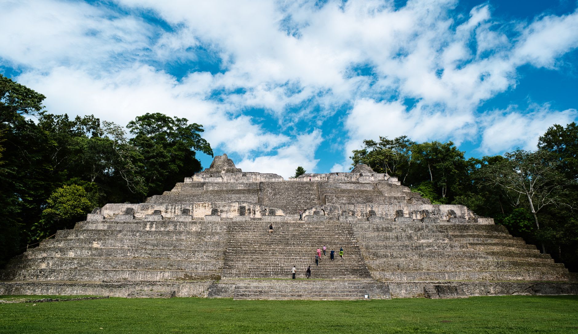The main plaza at Xunantunich spread below El Castillo, the Mopan River valley visible in the hazy distance beyond the jungle