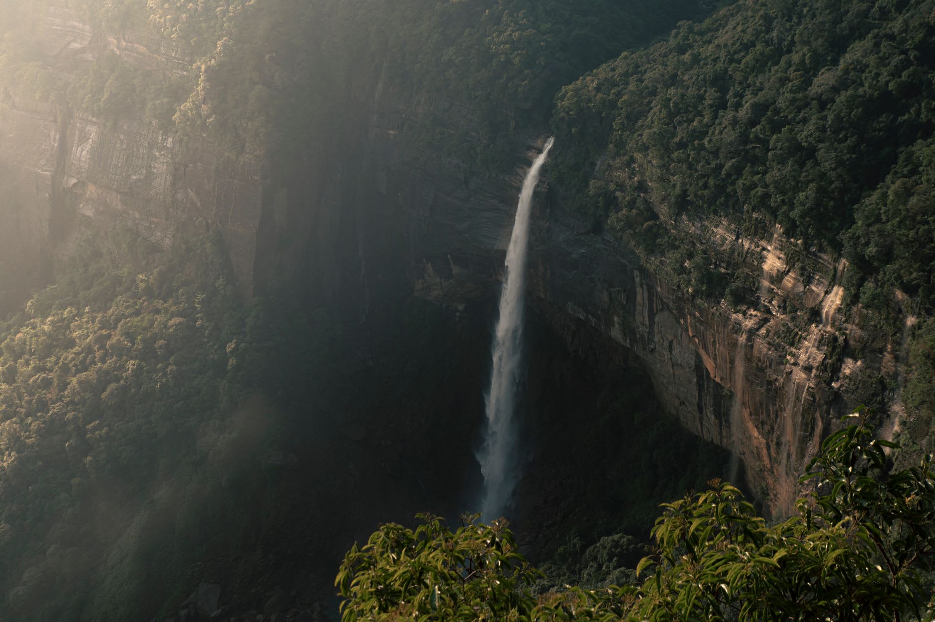 The Nohkalikai viewpoint looking down the full length of the falls, the white thread of water and the green pool far below visible between jungle-covered cliffs