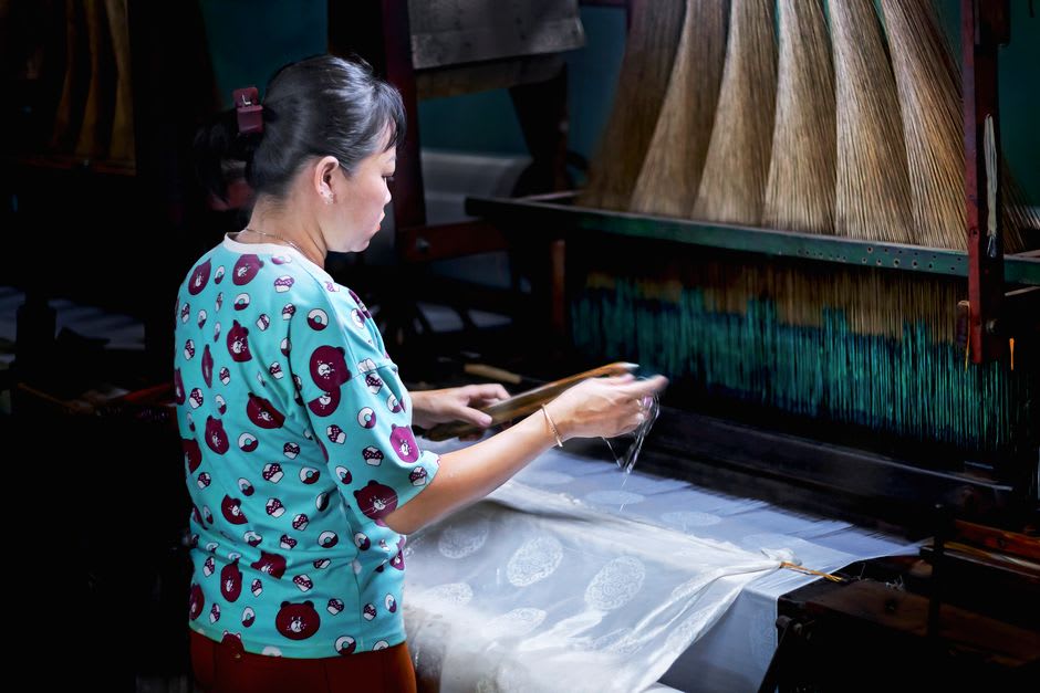 A weaver's hands guiding thread through a traditional wooden loom in Tan Chau