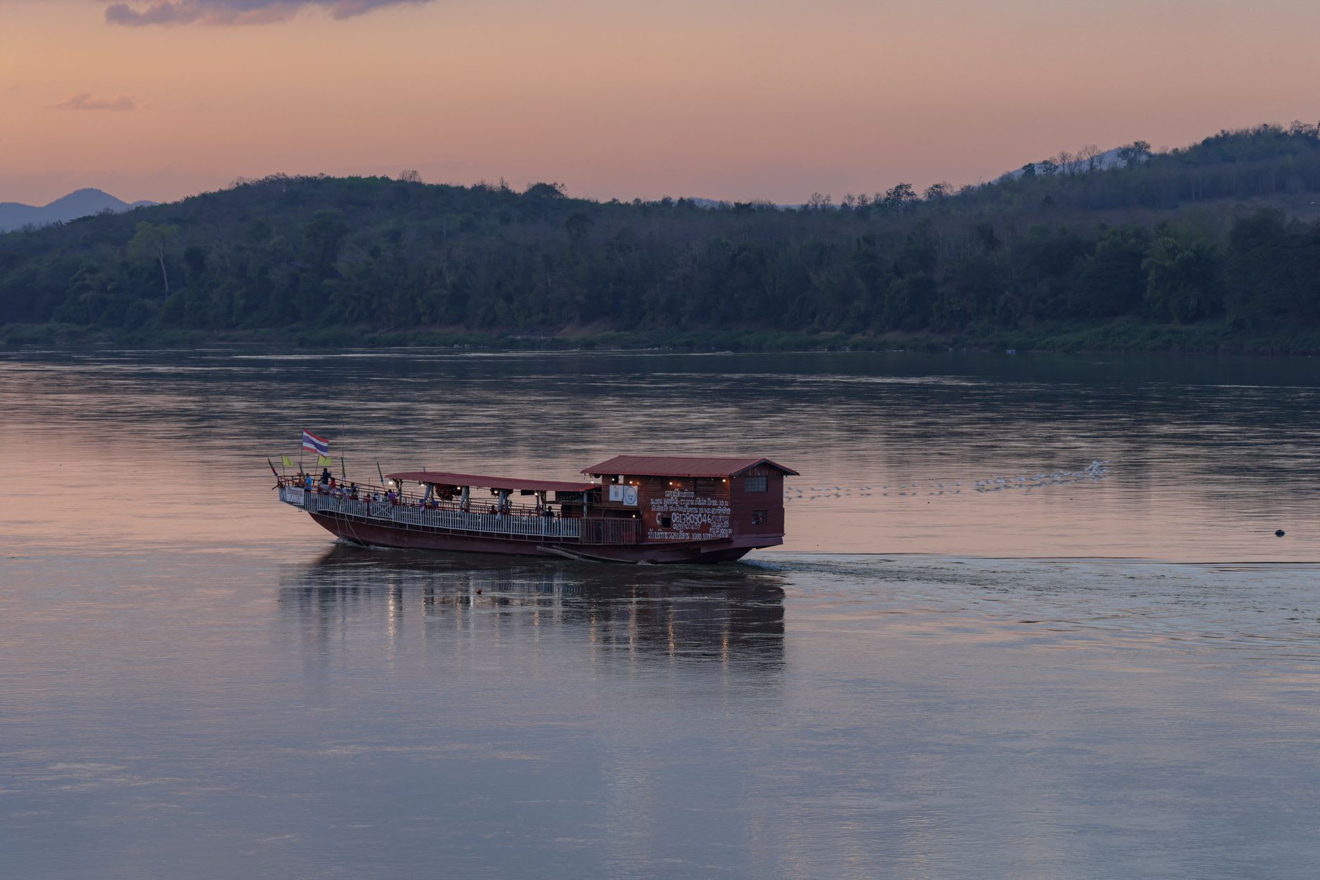 Fisherman in a long wooden pirogue casting a net on the calm Mekong off Don Khong, distant wooded islets behind him