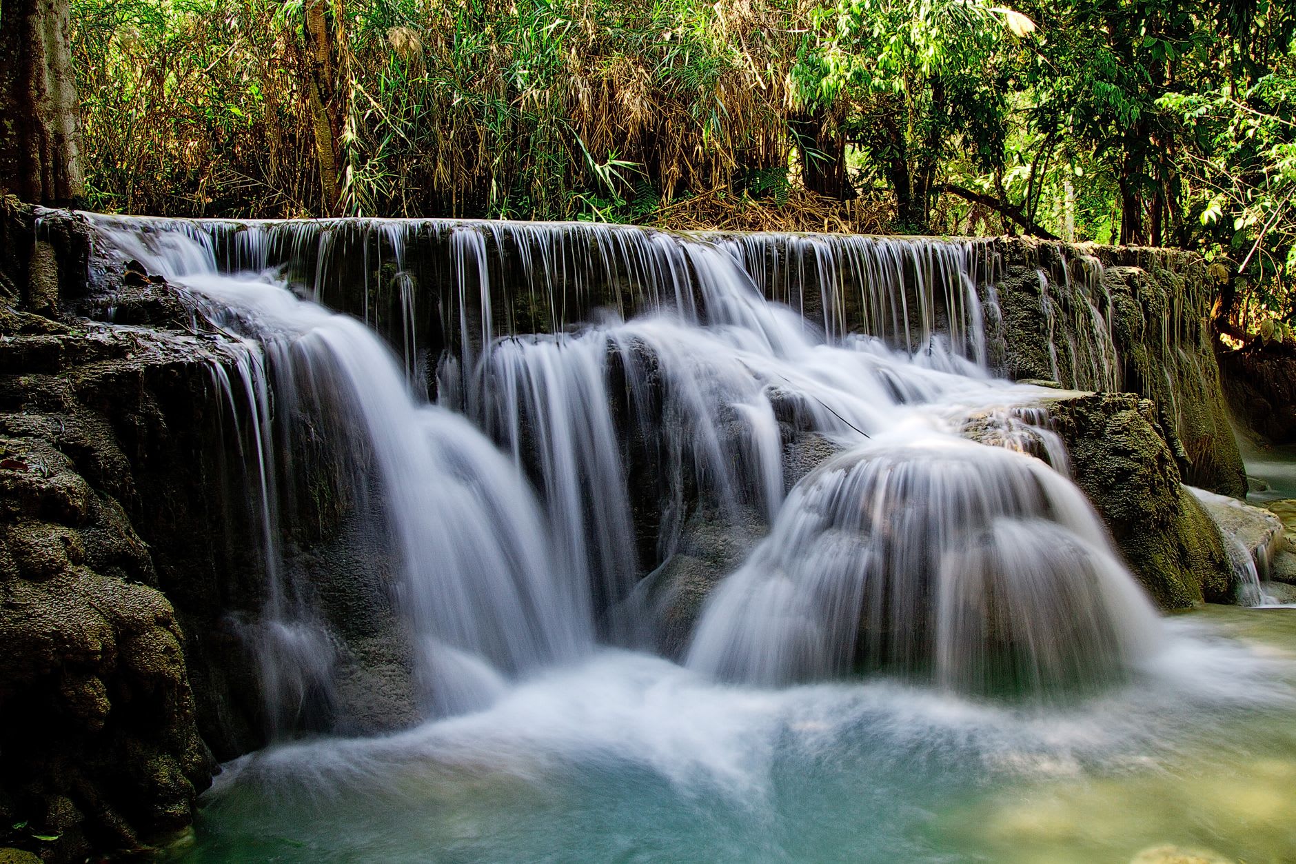Swimmers in the lower turquoise pools of Kuang Si Falls surrounded by jungle and limestone formations