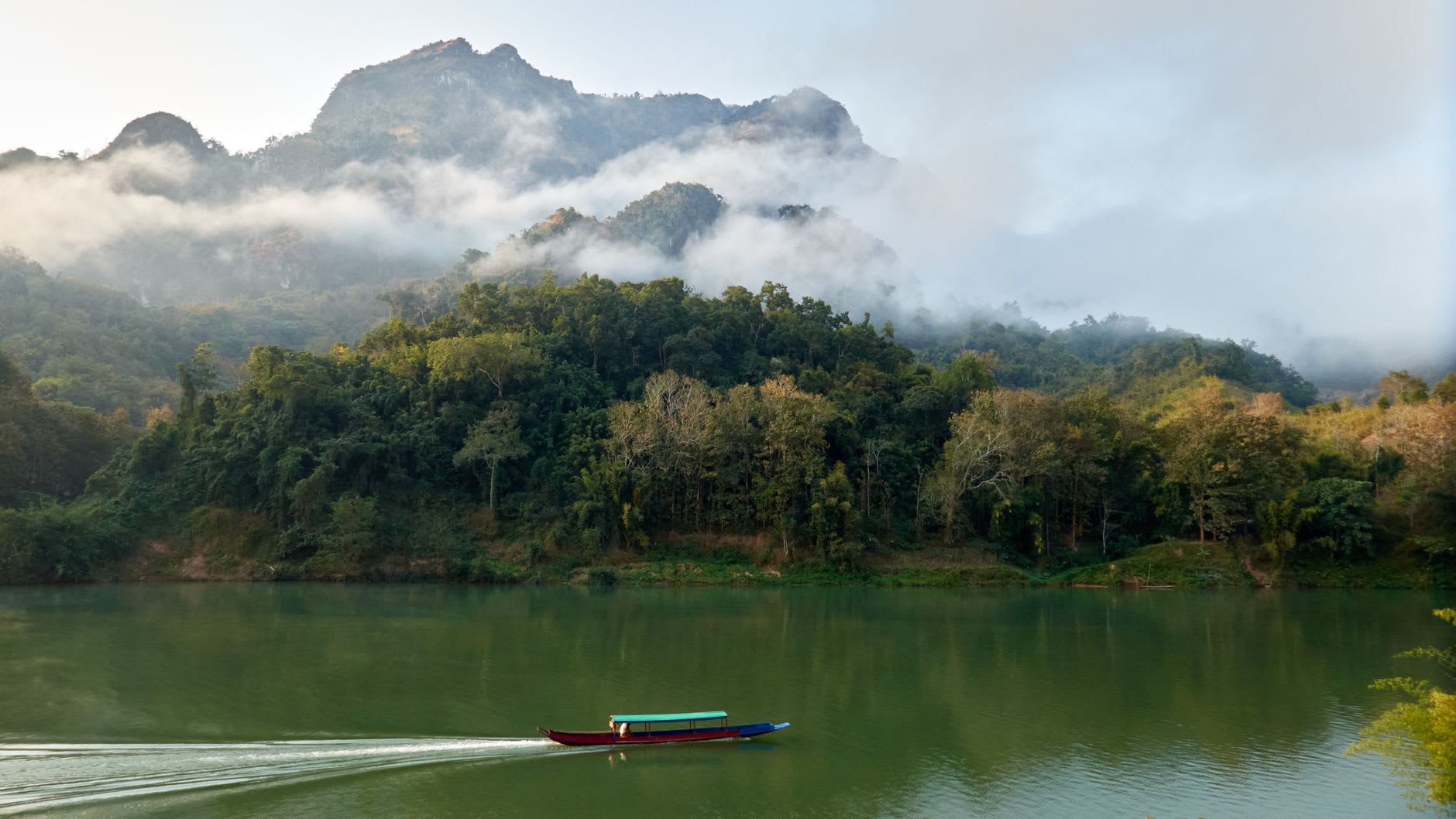 The Nam Ou River at the edge of Muang Ngoi Neua, limestone karst cliffs reflected in the still water at dawn