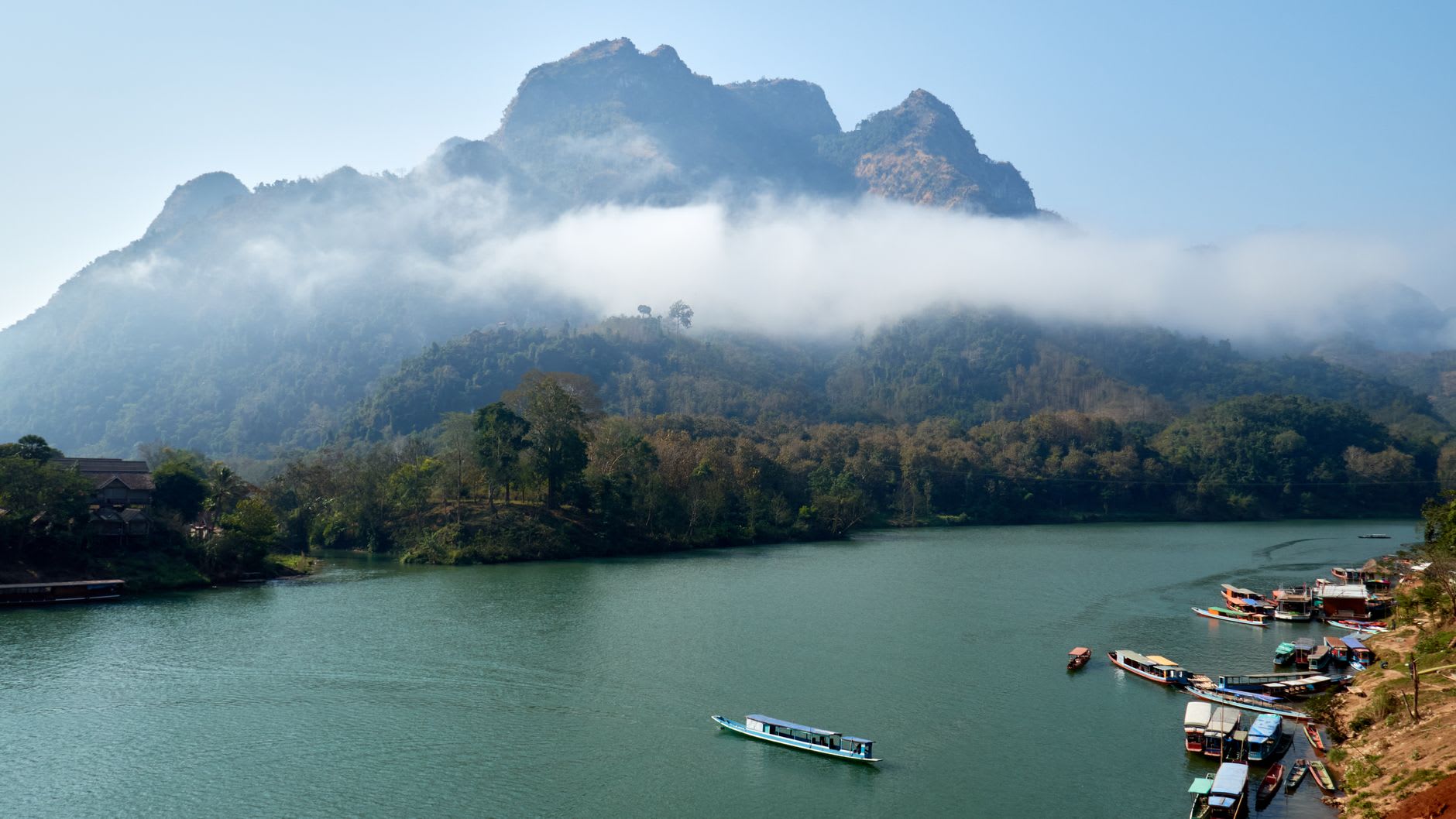 Morning mist rising from the Nam Ou River and between the limestone karst cliffs at Nong Khiaw, fishing boats visible below