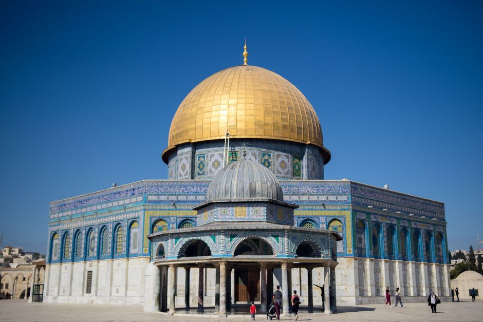 The rebuilt golden dome and minarets of the Al-Askari Shrine in central Samarra, pilgrims visible in the courtyard below