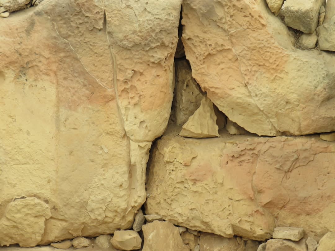 Une tranchée archéologique poussiéreuse à Uruk révélant des couches d'anciennes maçonneries et des fragments de poterie, les empreintes d'un gardien solitaire du site visibles au premier plan