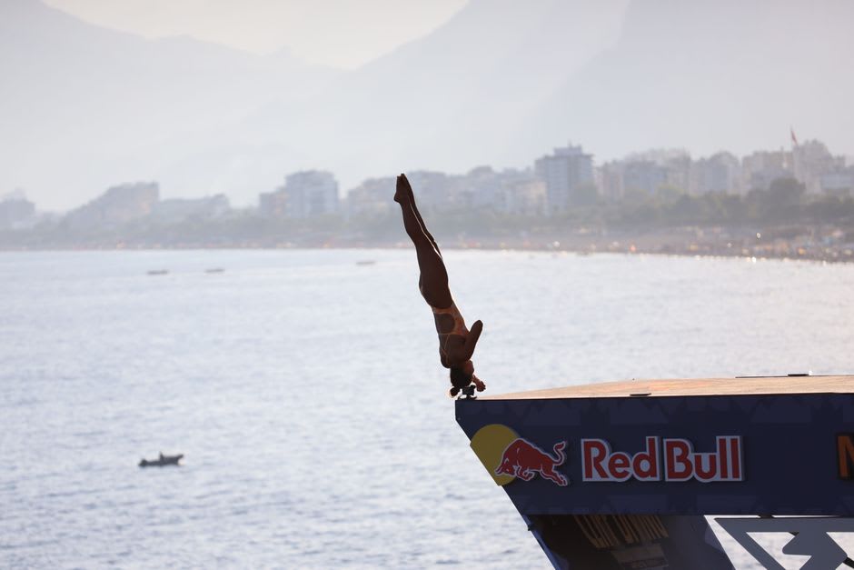 A clavadista cliff diver launching from the La Quebrada cliff in Acapulco, forty meters above the narrow Pacific inlet, arms spread, the waves below timing their arrival to receive him