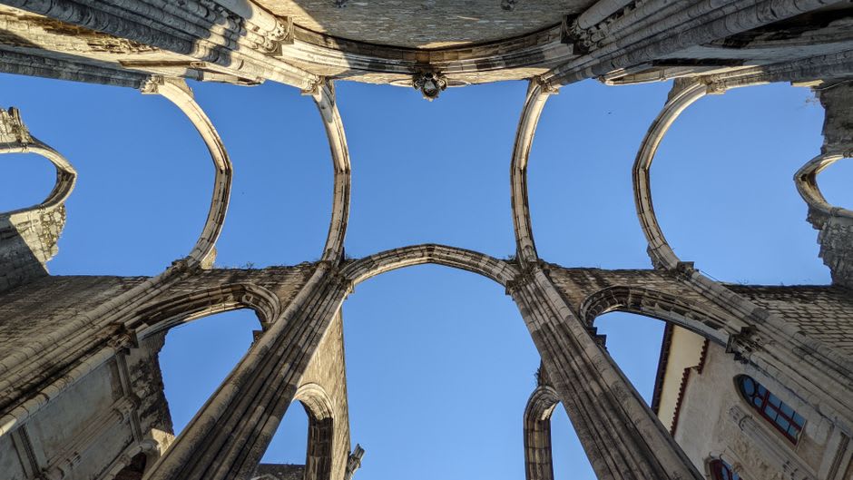 The interior of the open chapel of Actopan, its massive stone arch framing a view of the convent's stone facade and a blue sky beyond