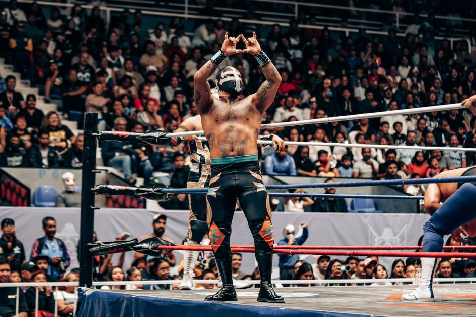 Lucha libre wrestlers in the ring at Arena México, one in a red and gold mask executing an aerial move over his opponent