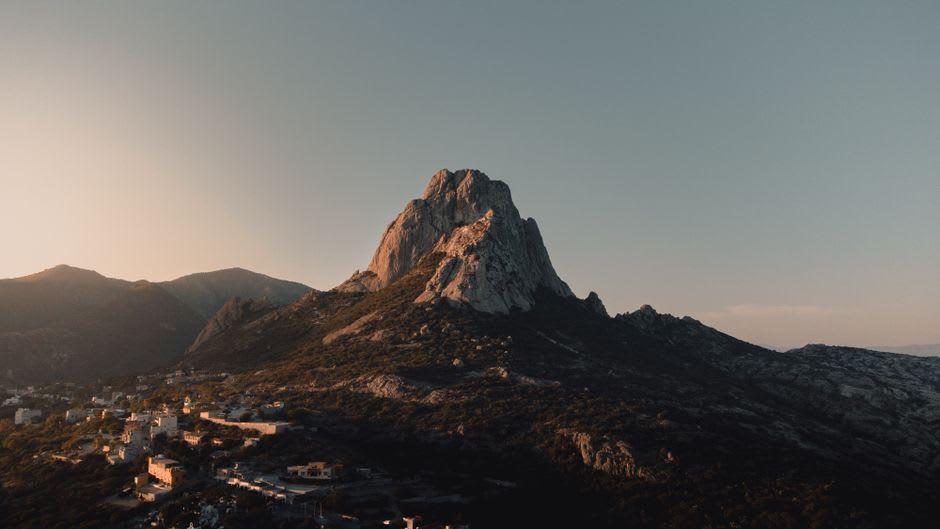 The Peña de Bernal monolith at dusk as a grey silhouette against the first stars, the quiet town lights below