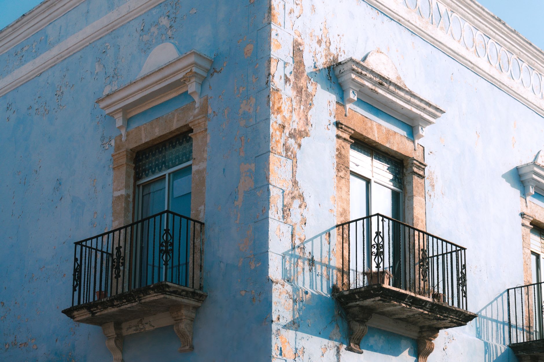 A row of painted colonial buildings on a narrow Campeche street, turquoise and ochre facades facing late afternoon sun