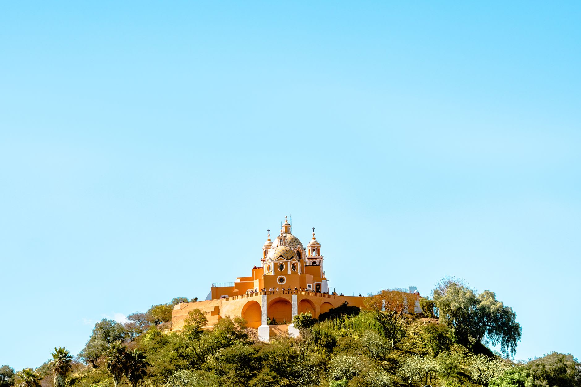 The grass-covered hill of the Great Pyramid of Cholula with the twin domes of the colonial church visible on the summit, Popocatépetl capped in snow behind