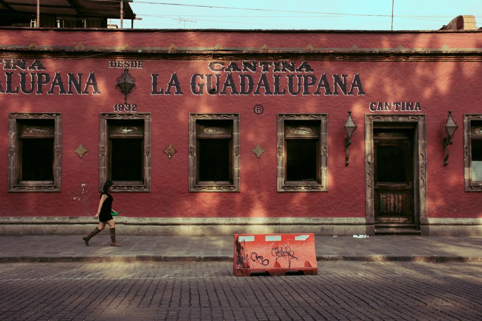 The arcaded portales of Comala's main plaza, white-painted columns hung with flowering plants, wooden tables and chairs outside the cantinas, free botana plates of sopes and tamales on the tables