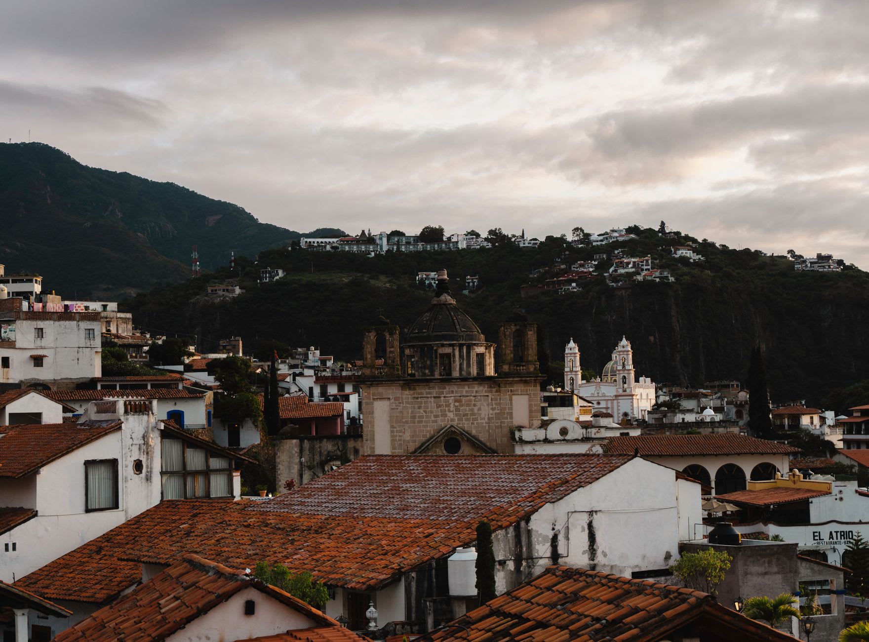 The view from the hillside above Copala down to the colonial plaza, the 18th-century church facade visible, stone-paved streets running between white colonial buildings, the Sinaloa sierra behind the abandoned silver mining town