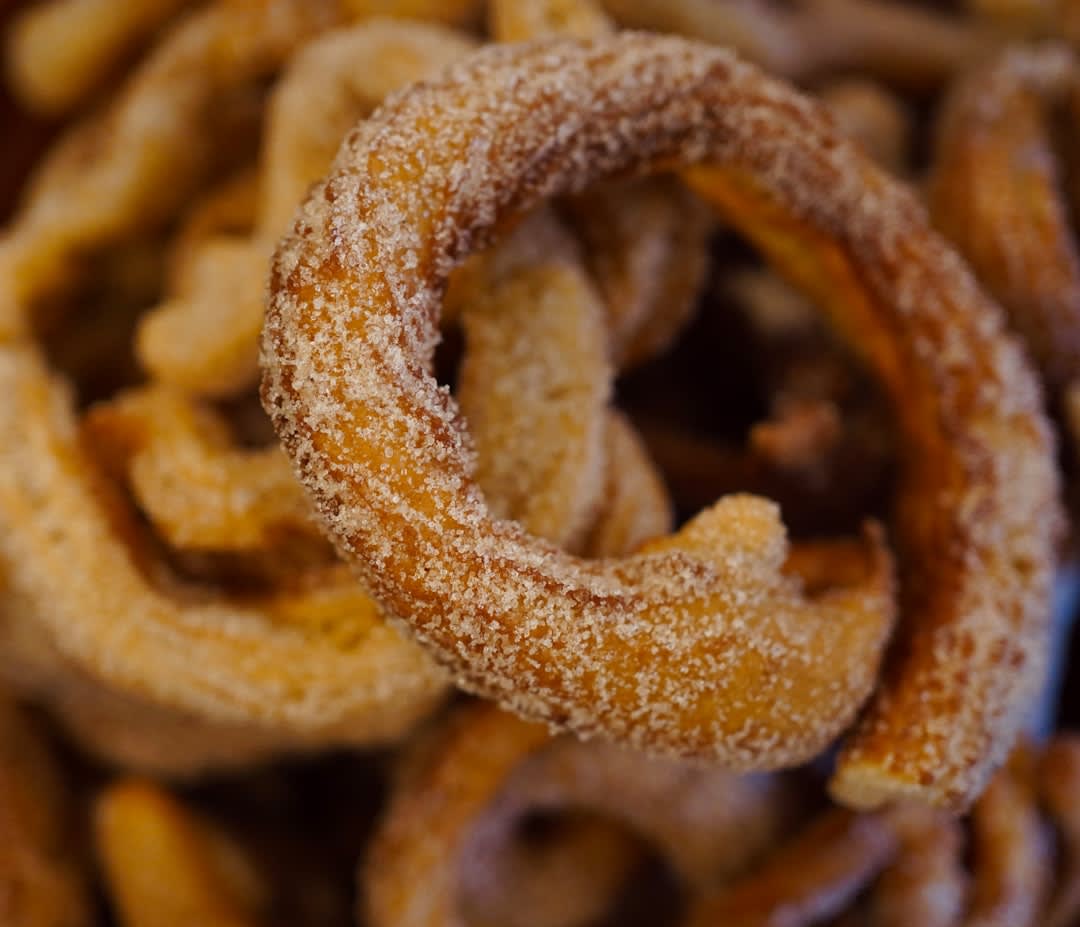 A plate of churros dusted in cinnamon sugar at a Coyoacán café table, a cup of thick hot chocolate alongside, the cobblestone street and colonial buildings visible through the window behind