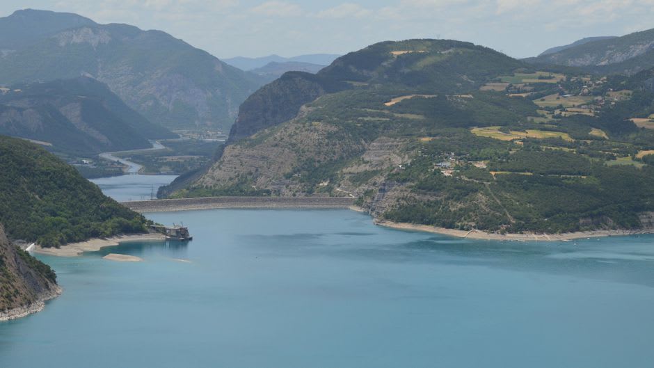 The Presa Palmito reservoir viewed from the dam wall, deep blue water between pine-forested canyon walls