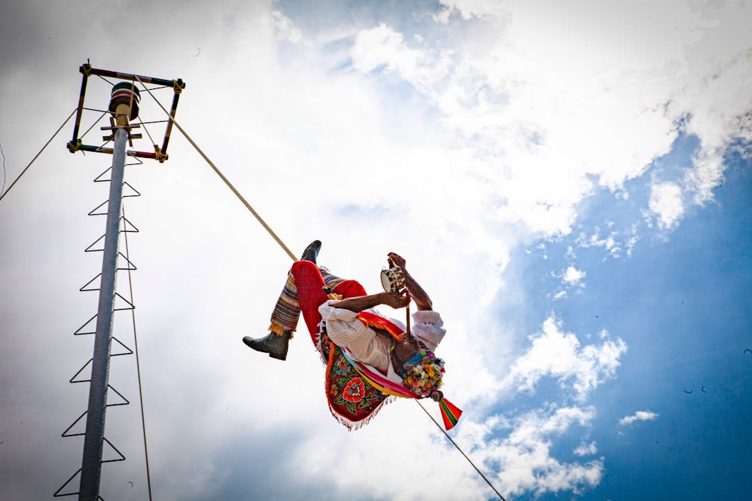 Four voladores descending in spiraling circles from a 30-meter pole at El Tajín, their rope-trailing bodies fanning out against the sky above the Totonac ruins, the jungle visible below