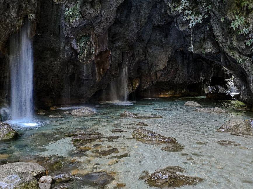 A lone swimmer floating in a turquoise thermal pool inside the grotto at Tolantongo