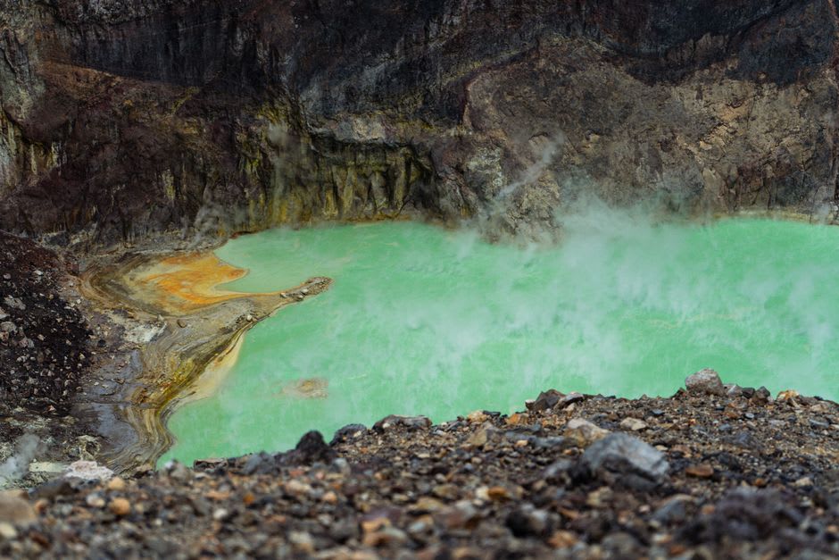 Thermal pool at Huandacareo with mineral-green water and steam rising toward the corrugated roof overhead