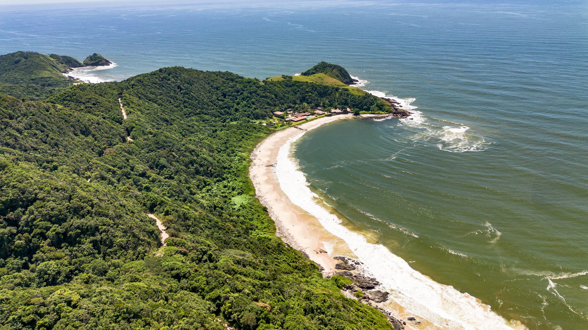 A secluded Huatulco bay seen from above, its turquoise water enclosed by jungle headlands, a crescent of white sand unmarked by any development