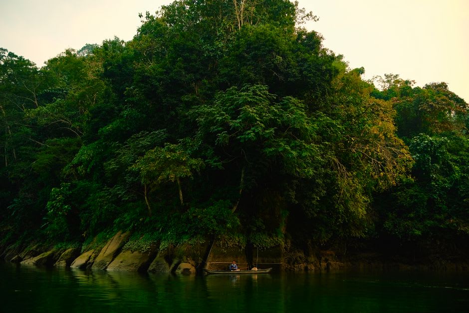 A flat-bottomed boat on the Usumacinta River with dense jungle riverbank, morning light on the water
