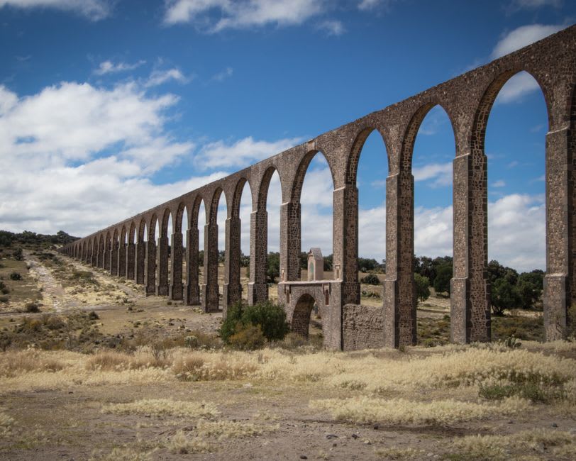 Old stone bridge over the Lerma River at La Barca, the arches reflected in the slow water below, ranchland stretching toward the Michoacán horizon
