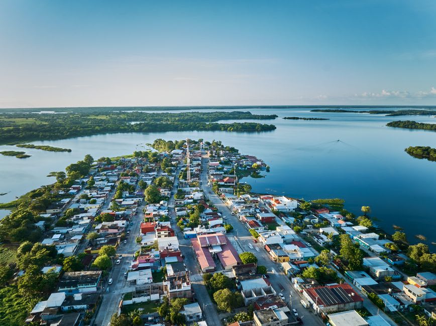 The village of Tziscao on the shore of its emerald-green lake in the Lagos de Montebello park, wooden houses of the Tojolabal Maya community at the water's edge, canoes on the still surface, the pine forest behind