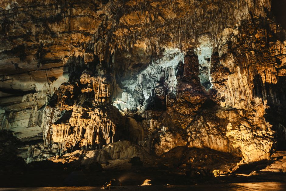 Cathedral chamber inside Grutas de Loltún with stalactites and light filtering through a natural opening in the vaulted ceiling above