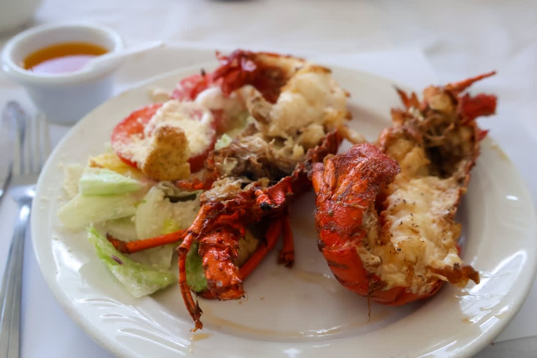 A plate of lobster tostadas on a wooden table at a palapa restaurant, Caribbean water behind