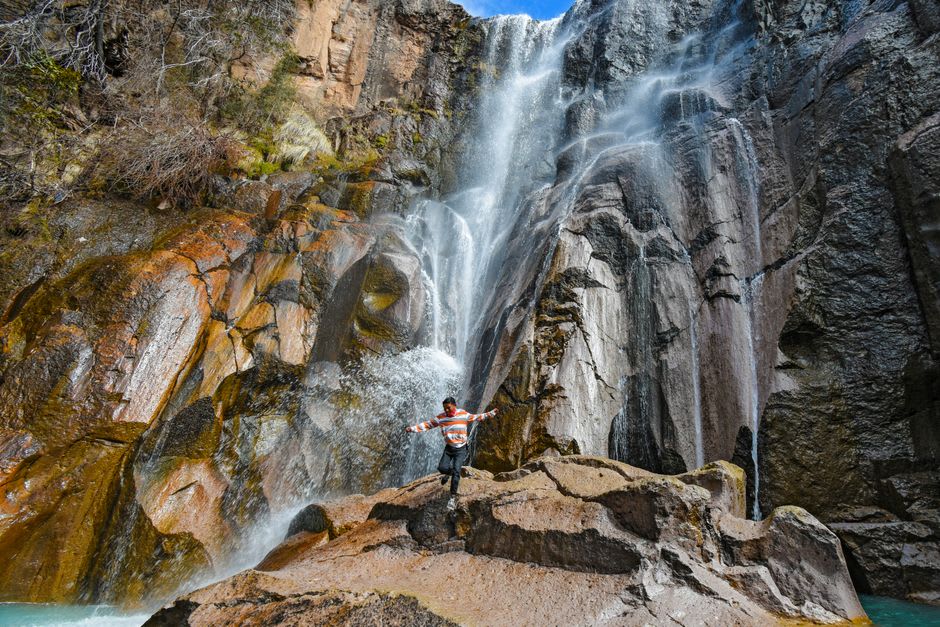 A swimmer floating in a crystal-clear pool at the base of a waterfall near Moris