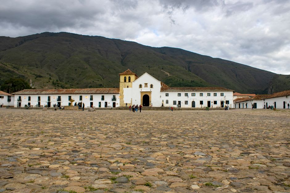 The main plaza of Naolinco in the morning, the colonial church behind, fog still filling the gorge below the plaza edge, pine trees on the slope above