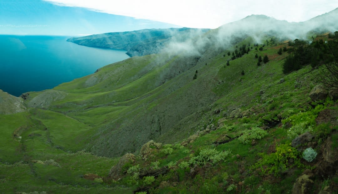 A quiet street in the Nahua town of Naupan, low houses along a steep wet lane, mist settling over the green mountainside, a woman in traditional embroidered dress walking uphill