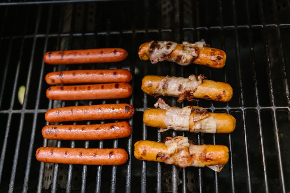 A Sonoran-style hot dog wrapped in bacon resting in a bolillo bun with beans, tomato, and condiments