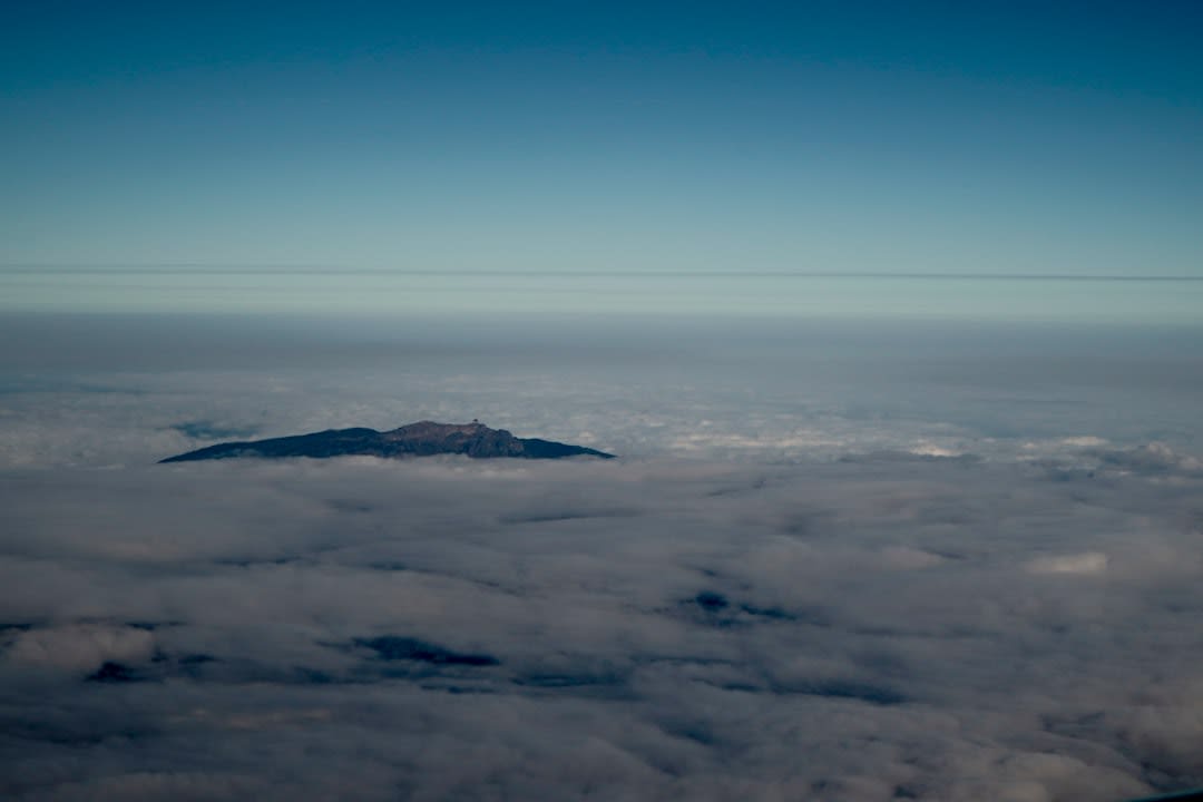 A mountaineer on the upper snow slope of the Pico de Orizaba, the glaciated summit cone above, the mountain's 5,636-meter peak catching the first light of dawn, the cloud sea far below covering the Veracruz lowlands