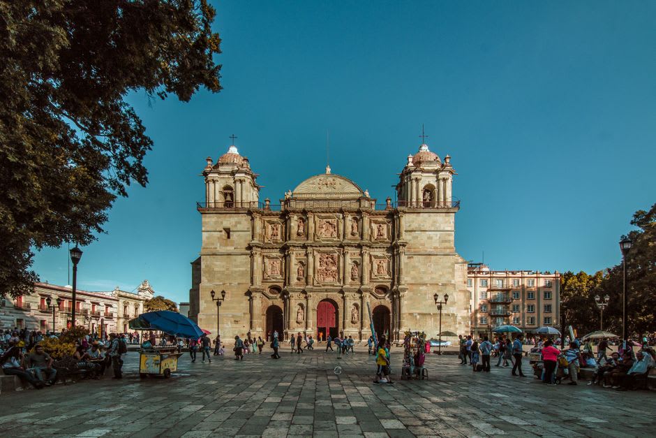 The plaza of Pabellón de Arteaga in late afternoon, the church facade at the far end, vendors and benches in the foreground shade