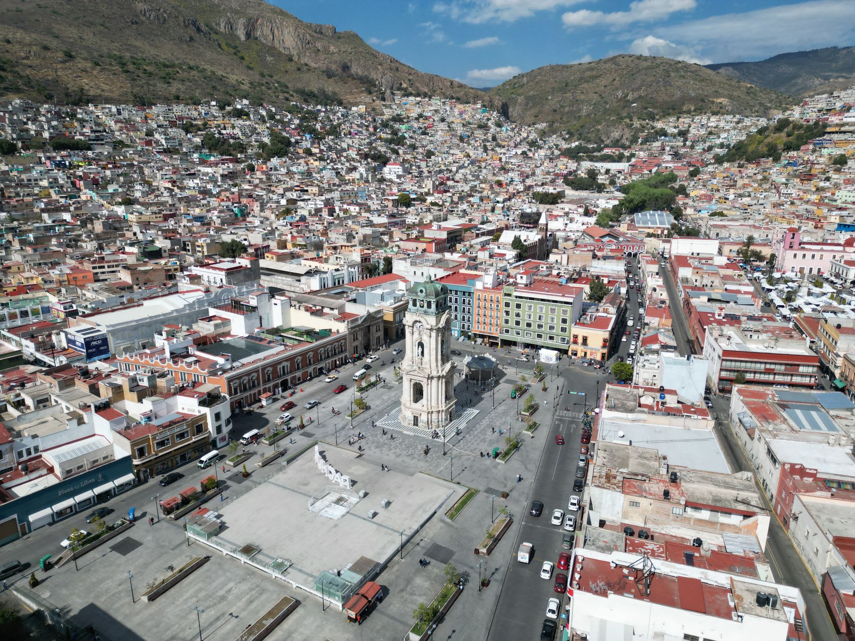 An Pachuca paste vendor's cart near the Reloj Monumental, the pastries lined up under a cloth, their crimped tops visible, a hand reaching for one, the clock tower visible behind in the late morning light