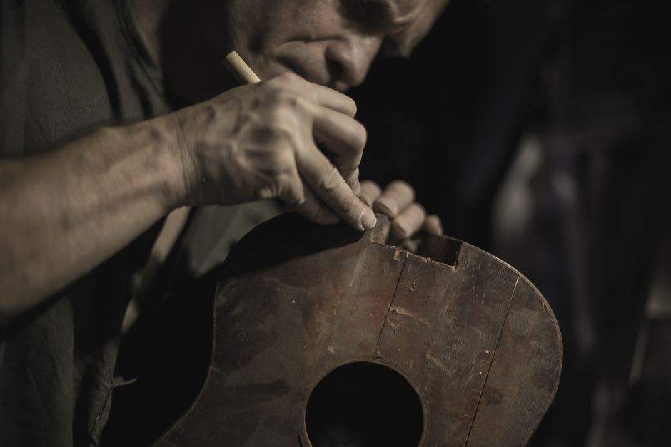 Luthier hands shaping a guitar neck in a Paracho family workshop, cedar shavings curling across the workbench
