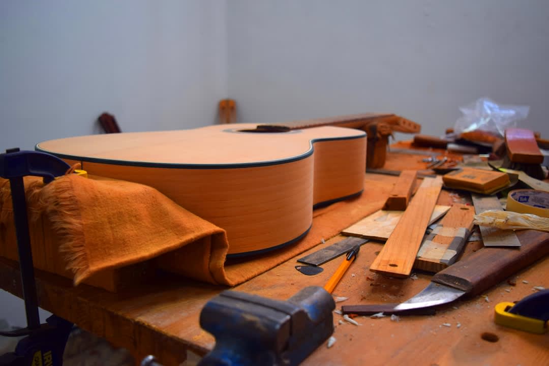A finished classical guitar from a Paracho master luthier, the cedar soundboard with its intricate mosaic rosette visible, the rosewood back and sides, displayed on a wooden stand in the workshop, the Paracho street visible through the doorway behind