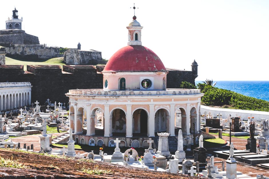 The partially buried nave of the church of San Juan Parangaricutiro, the stone walls rising from the black lava field, carved doorways at eye level, offerings and flowers at the base of the tower