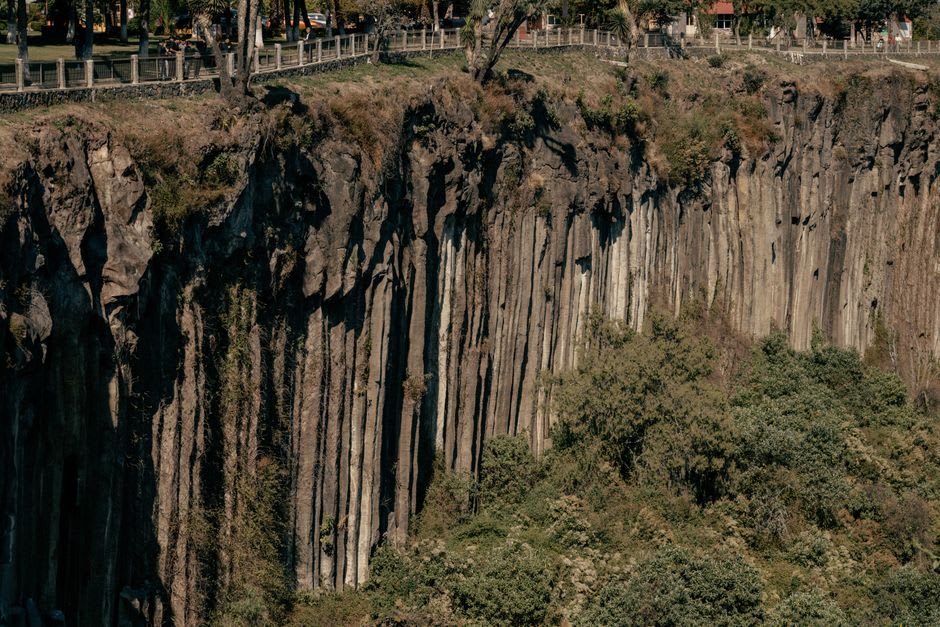 Volcanic basalt columns rising from fir forest in Mexiquillo, mist moving through the trees in the background