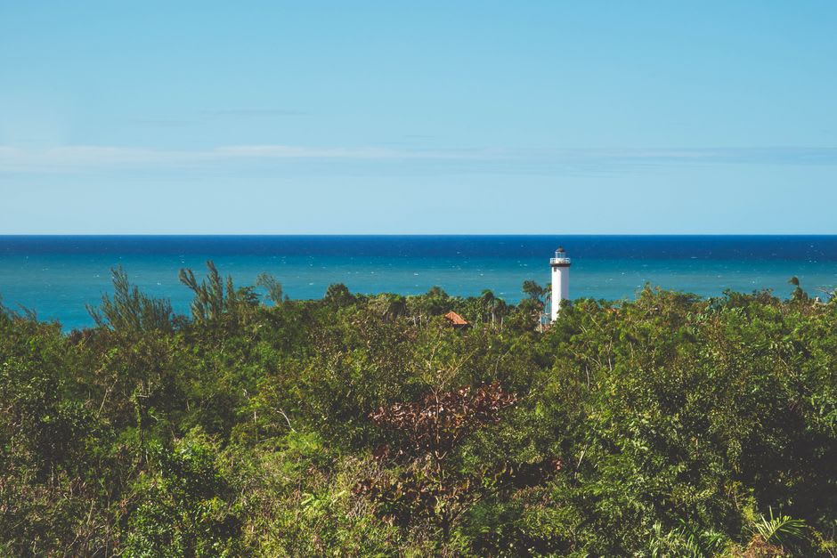 The leaning lighthouse of Puerto Morelos photographed from the main plaza, tilted against a blue Caribbean sky with bougainvillea in the foreground