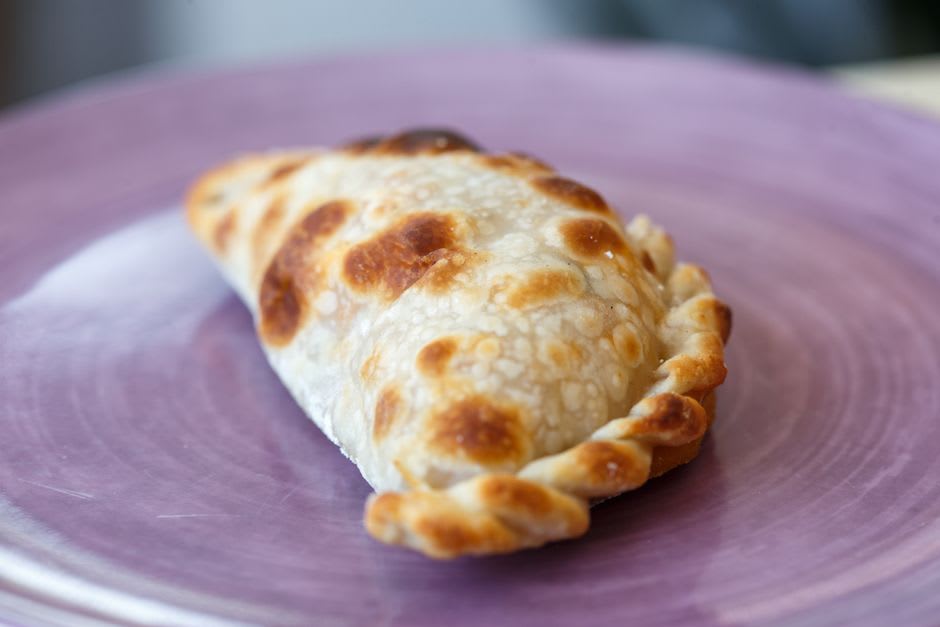 A selection of pastes — Mexico's version of the Cornish pasty — from a Real del Monte bakery, the semicircular pastries split to show their fillings of mole negro, tinga de pollo, and cheese with rajas, on a wooden board