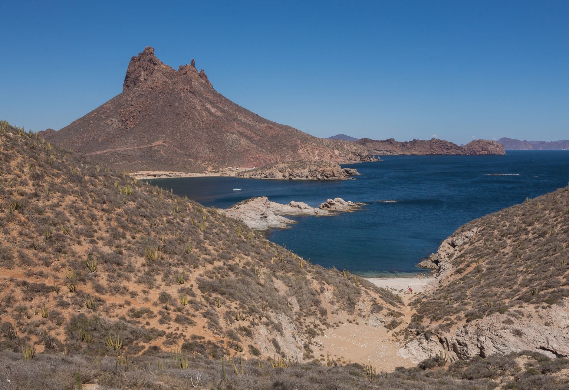 The view from near the Tetakawi peak summit looking down over San Carlos bay, the turquoise water enclosed by black volcanic hills, the distant Guaymas visible to the southeast