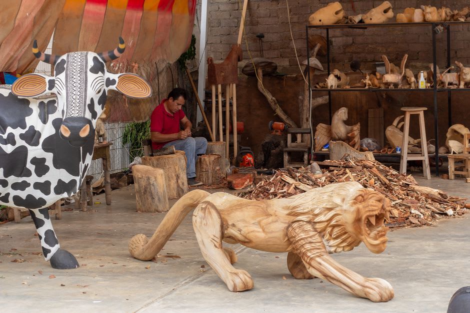 Artisan hands painting fine geometric patterns onto a carved wooden alebrije in a Tilcajete family workshop