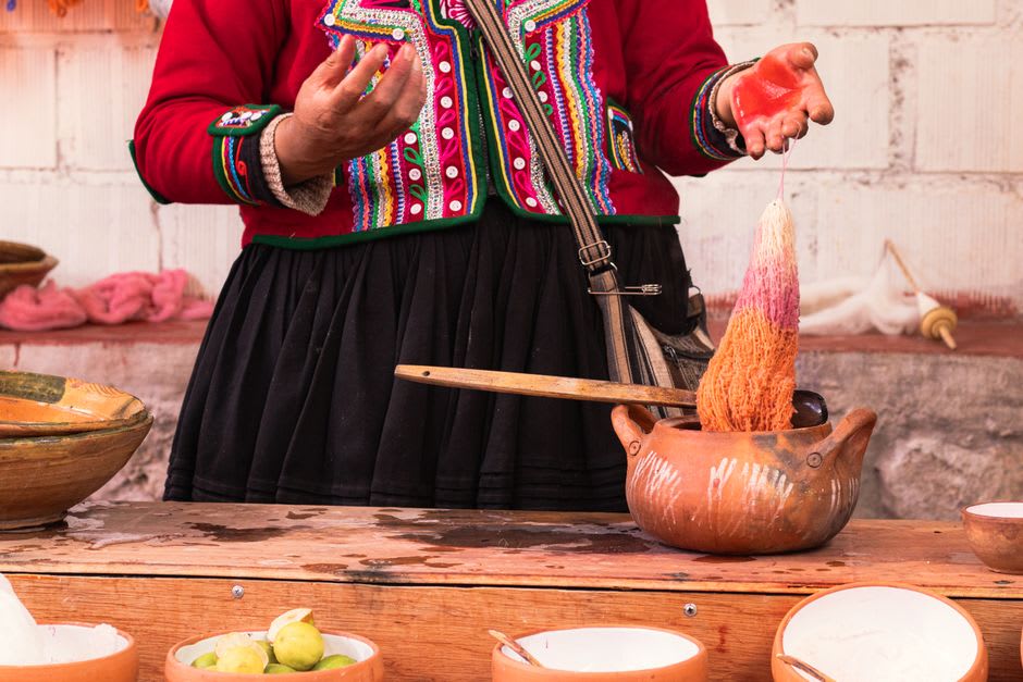 The natural dye demonstration at a Teotitlán del Valle workshop, a skein of wool lifting from a cochineal dye bath in deep crimson red, dried cochineal insects and plant material on the table, the weaver explaining mordanting