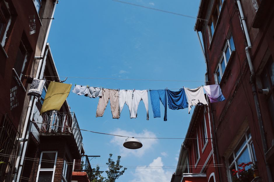 A view along a Tepito street in morning light, apartment buildings hung with laundry, a taquería open on the ground floor, pigeons on the power cables overhead