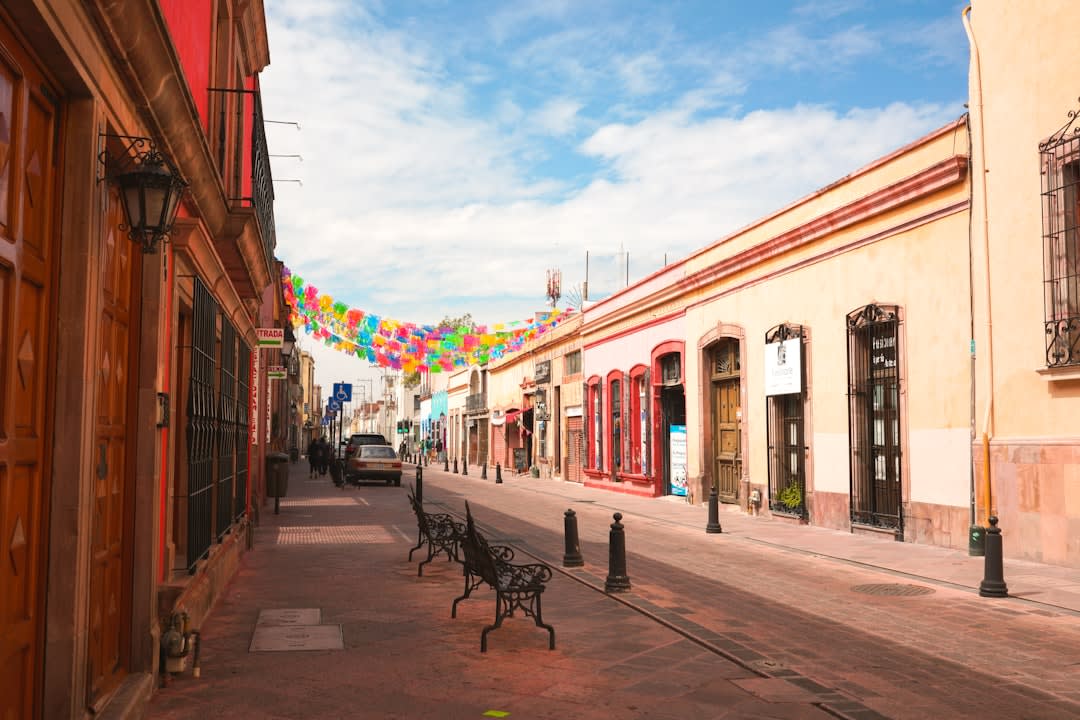 A quiet cobblestone lane in Tepoztlán lined with painted adobe walls and bougainvillea, the forested cliffs visible at the end of the street