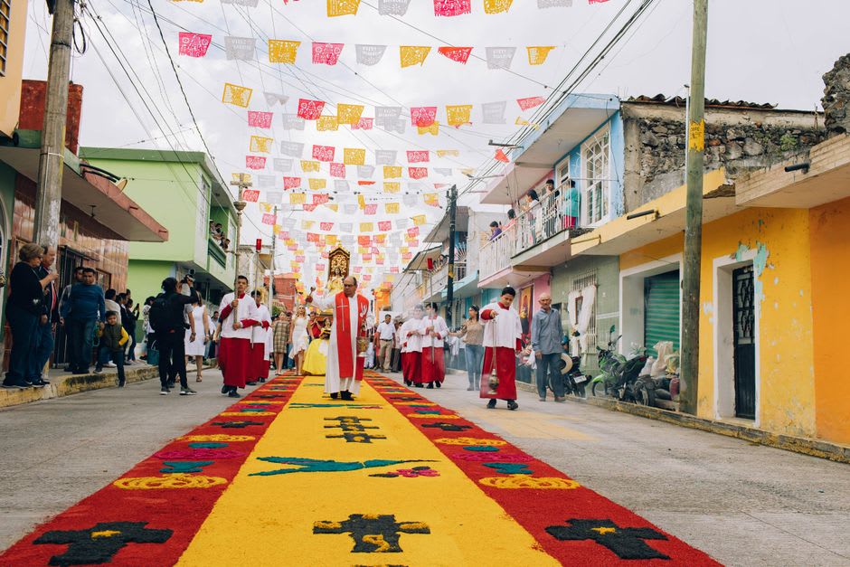 The Candelaria festival procession on the Papaloapan River, decorated boats carrying the image of the Virgin, crowds on the Tlacotalpan riverbank, the pastel facades of the town behind, confetti in the air