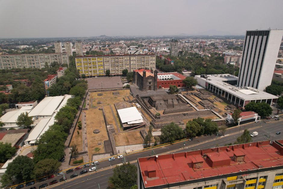 The Aztec pyramid platforms of Tlatelolco's ceremonial center, grey volcanic stone in low morning light, the colonial church of Santiago visible behind